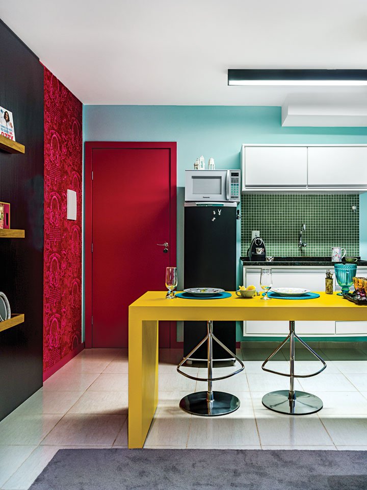Um amplo tapete neutro (D Design) delimita toda a área do home e quarto e a bancada em laca amarela setoriza a cozinha.