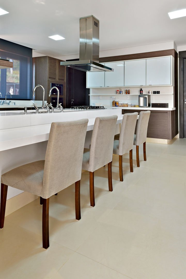 A cozinha traz mobiliário em lâmina de madeira natural e vidro e bancadas em Solidus branco, da Brich.