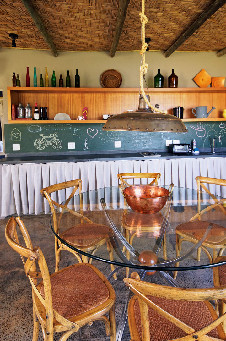 A mesa de jantar com tampo de vidro e cadeiras de madeira (Depósito Casa Mix) foram posicionados sob o pendente industrial 