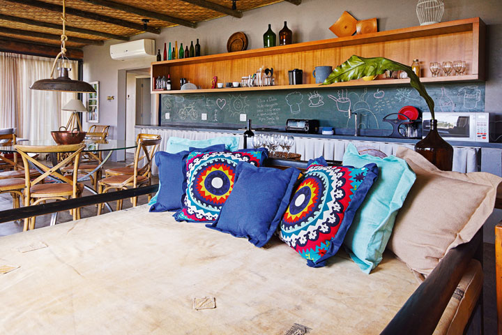 A cozinha integrada ganhou uma lousa para recados. O banco de madeira com almofadas coloridas (Depósito Casa Mix) tem profundidade de cama e permite acolher o casal deitado para uma soneca após o almoço