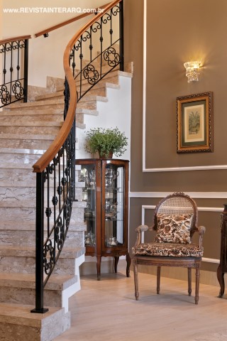 A sinuosa escada com degraus em mármore e guarda-corpo de ferro (Quality Inox) é a estrela do hall de entrada. A pintura escura com detalhes claros valoriza as boiseries