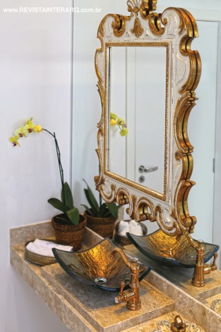 Metais e espelho dourados foram a escolha para o lavabo com bancada em mármore Travertino
