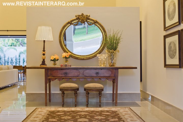 O móvel antigo, com banquetas e espelho redondo e o tapete estampado recebem com sofisticação quem chega à residência