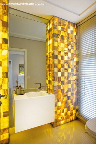 Os mosaicos de ônix iluminado emolduram a bancada em Silestone (Marmoraria Gran-Norte) do lavabo