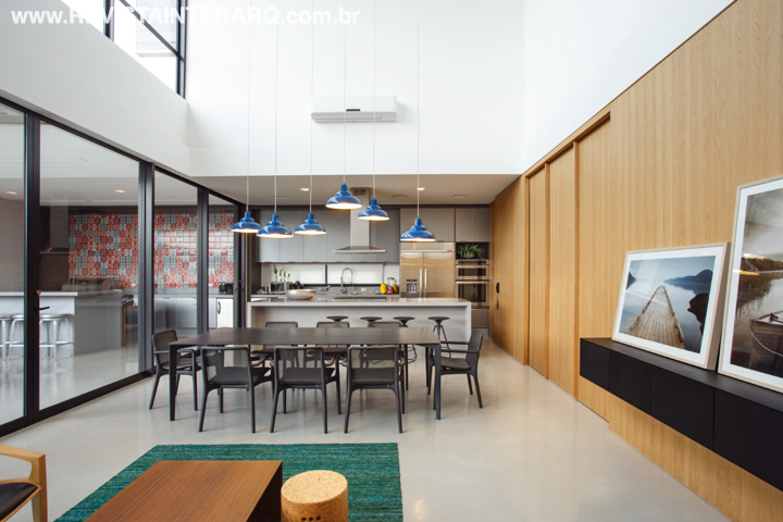 Também integrada ao social, a cozinha chama atenção com a composição de luminárias industriais azuis e mesa preta