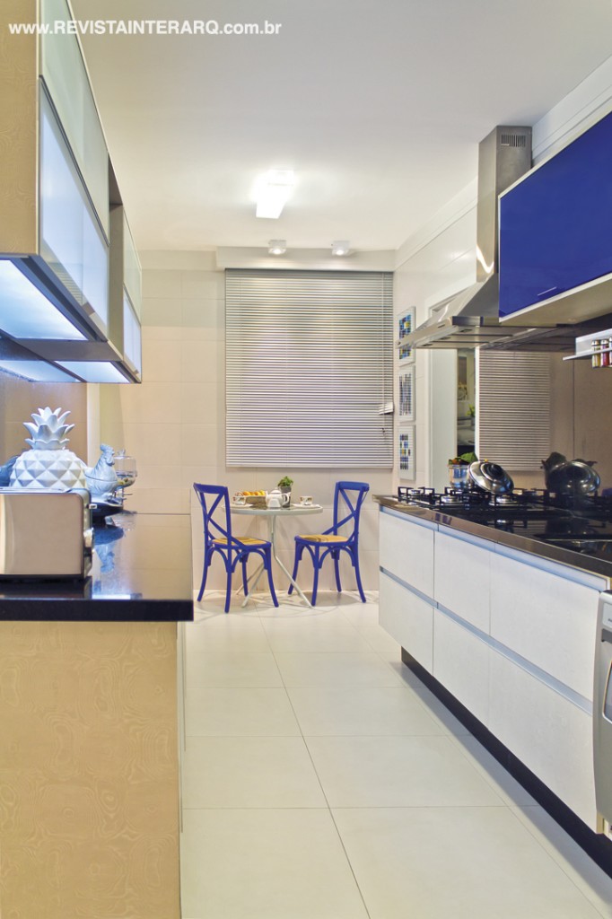 A cozinha tem piso em porcelanato claro e armários planejados com acabamento branco e azul (Dell Anno). No canto, mesinha e cadeiras (Trevizan Center) para lanches rápidos