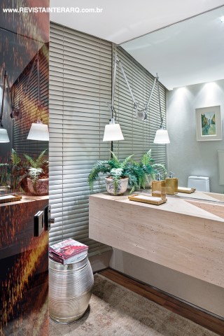 O lavabo traz bancada em mármore Travertino Romano Bruto (Silestone), tapete oriental (By Side), garden seat de metal e luminária articulável Tolomeu