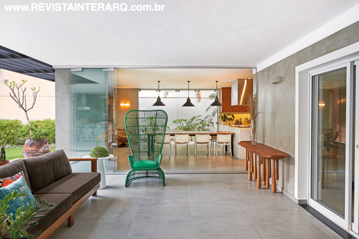 A varanda, com estar e área gourmet, tem base cinza para ressaltar as cores e formas de design, como a poltrona verde Monalisa junto à mesa lateral e ao aparador de madeira