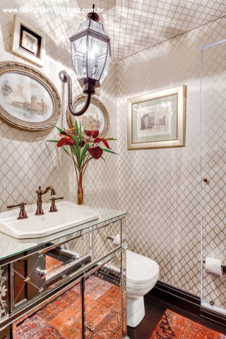 O papel de parede também foi usado no teto do lavabo, que tem uma área de banho camuflada. A arandela imponente faz às vezes de lustre e a bancada espelhada dá profundidade ao ambiente. Quadros da Cristina Lemos