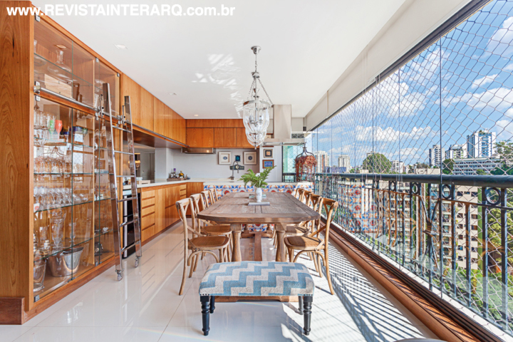 O espaço gourmet, na varanda, é setorizado pelo móvel planejado com painéis de madeira e cristaleira. Mesa e pufes garantem o ar mais despojado