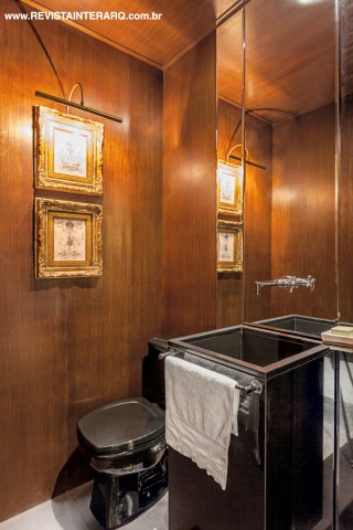 Todo revestido com painéis de madeira, o lavabo evoca classe e sofisticação com a cuba em peça única, espelho e tela com moldura dourada da Marizza Prado