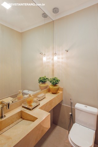 No lavabo, a bancada em mármore Crema Marfil tem cuba esculpida. O papel de parede suave (ACB Casa) é duplicado pelo espelho. Iluminação da Luminá Iluminação