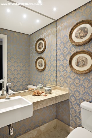 O lavabo contam com paredes espelhadas e piso em mármore. O papel de parede adamascado em azul e dourado (ACB Casa) remete ao luxo