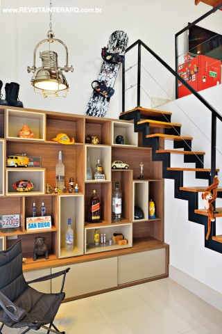 O quarto do filho tem estilo loft, com dois pavimentos e uma estante com formas ousadas junto à escada de ferro com pisantes de madeira. A cadeira é da UneRobusti