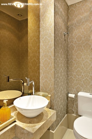 O lavabo traz papel de parede dourado adamascado (ACB Casa), bancada em mármore Crema Marfil e louças da Duo