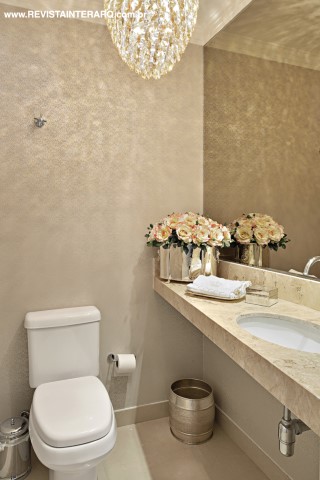 A tonalidade da bancada em mármore Crema Marfil (Marmoraria Exclusive) norteou a escolha do papel de parede (ACB Casa), do lustre (Luminá Iluminação) e do arranjo floral do lavabo