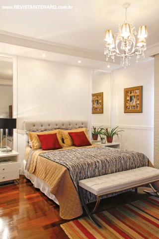 Emoldurada por espelhos e criados em laca (UneRobusti), a cama do casal conta com enxoval em tonalidades neutras. O piso de madeira agrega conforto. Luminotécnica da Luminá Iluminação
