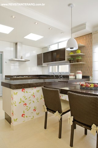 A cozinha interna faz contraponto à sala de almoço com papel de parede com estampa de maçãs (ACB Casa). As cadeiras em alumínio e fibras sintéticas são da Copav