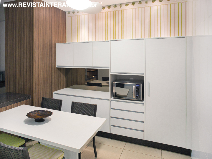 A cozinha tem painéis amadeirados, armários planejados em laca branca e metais da Duo