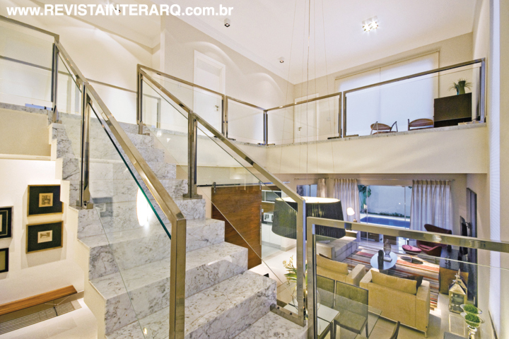 A escada que leva ao piso superior é em mármore Carrara. A altura do pé-direito da sala de jantar, integrada ao living, é enfatizada pelo pendente com fitas de voil de seda, feito sob encomenda (Luminá Iluminação)