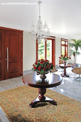 A composição com mesa em madeira (Robusti), lustre de cristal e tapete oriental marca o hall de entrada