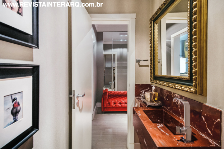 O lavabo tem cuba esculpida na bancada em mármore Rojo Alicante e espelho com moldura trabalhada