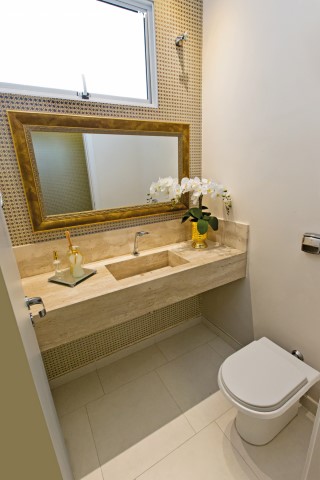 Bancada em mármore Travertino, espelho com moldura (Vidraçaria Colorado) e papel de parede claro compõem o lavabo