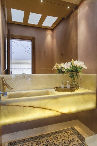 Os protagonistas do lavabo são a bancada em ônix com iluminação embutida e a torneira com design de Philippe Starck