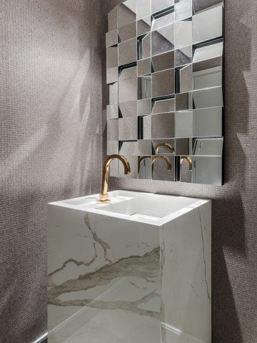 O lavabo mescla a textura do mármore e o brilho do cobre com o jogo de espelhos