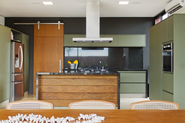 A cozinha com armários na cor verde oliva, bancadas em granito preto e madeira de demolição