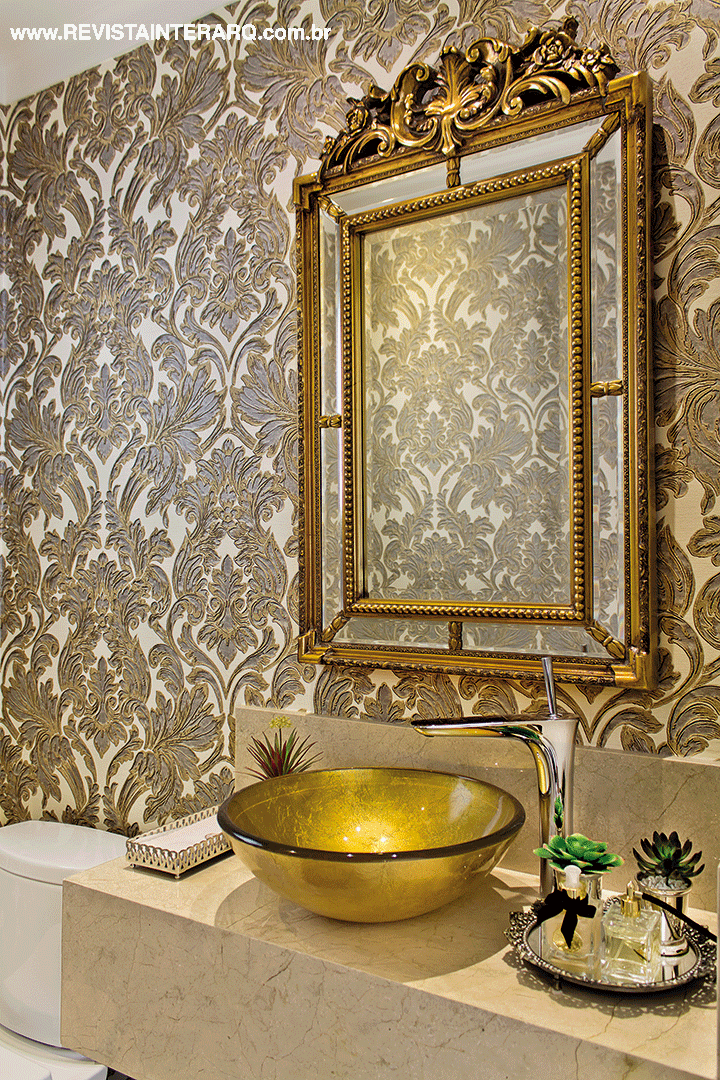 O papel de parede adamascado (Griffe A) acompanha a bancada em mármore Crema Marfil com cuba dourada. O espelho é da Vera Orsi