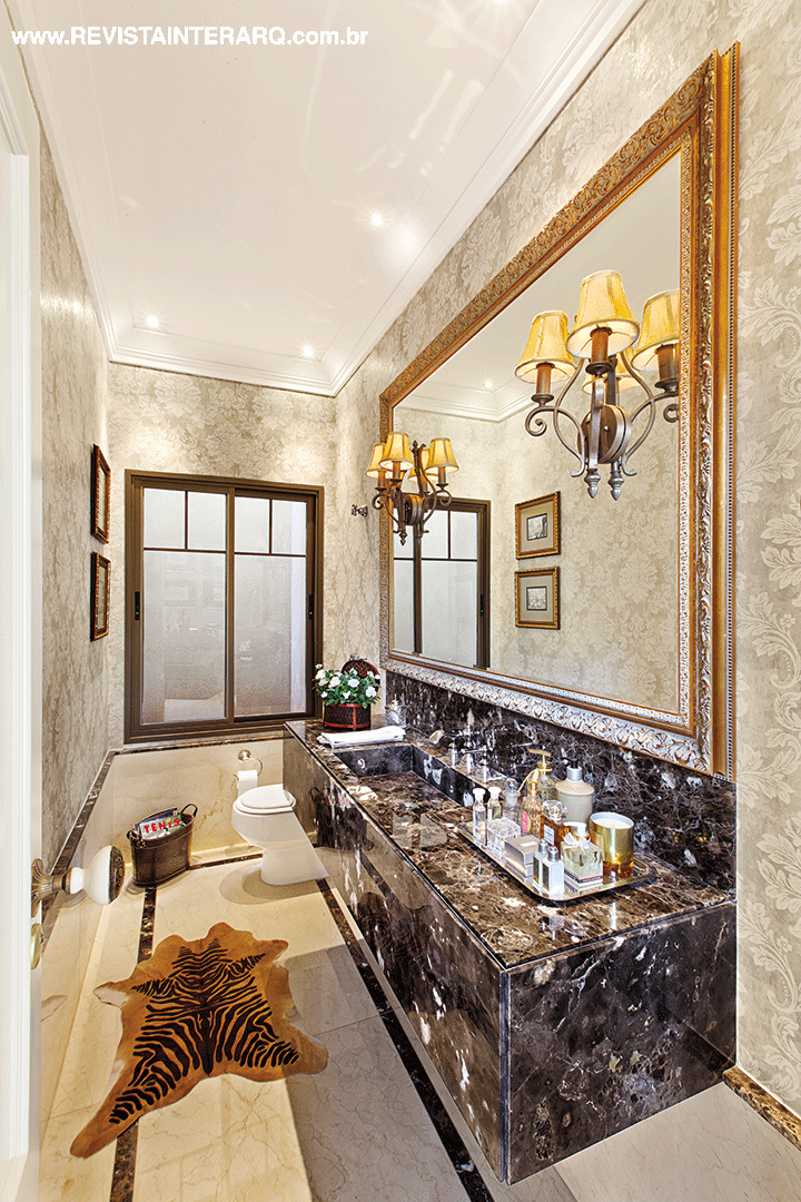 No lavabo, o espelho com moldura dourada acompanha toda a bancada em mármore Marrom Imperial