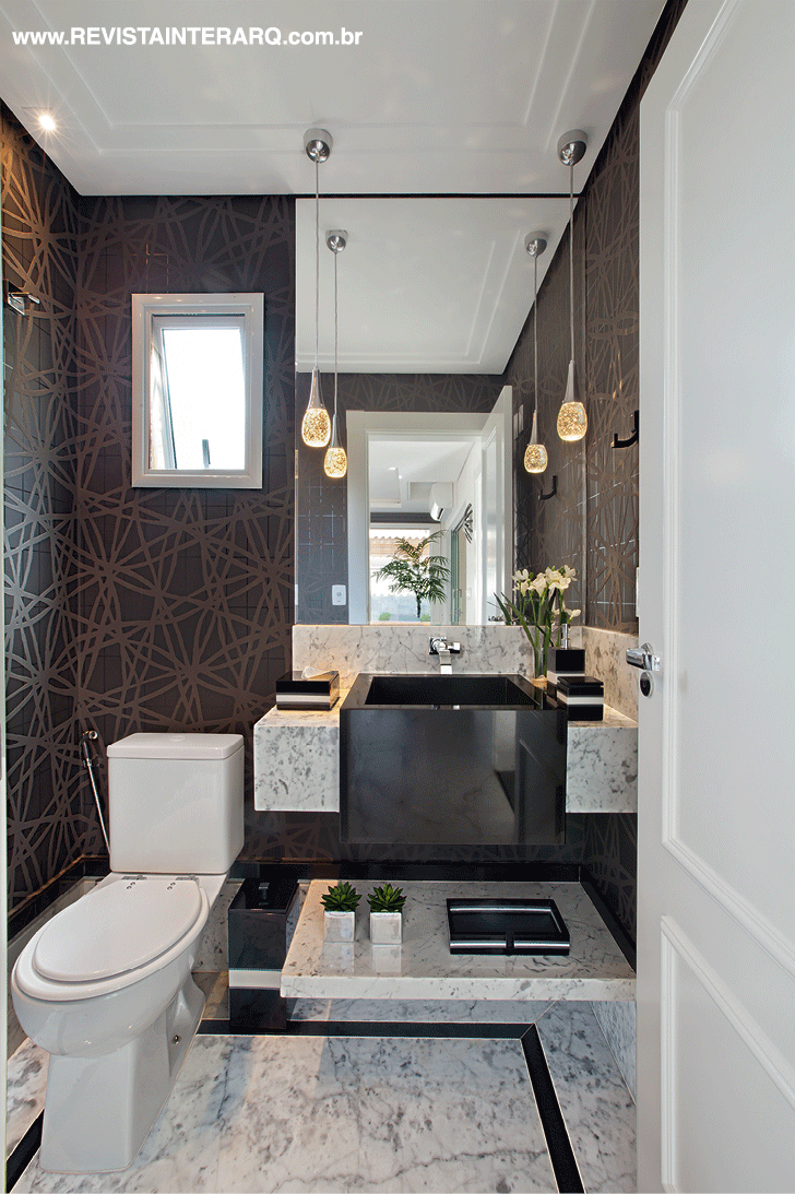 O lavabo apresenta o contraste do papel de parede escuro (Griffe A) com o piso e a bancada em mármore Carrara (Marmocruz Mármores e Granitos). Louças e metais da Ornamentare