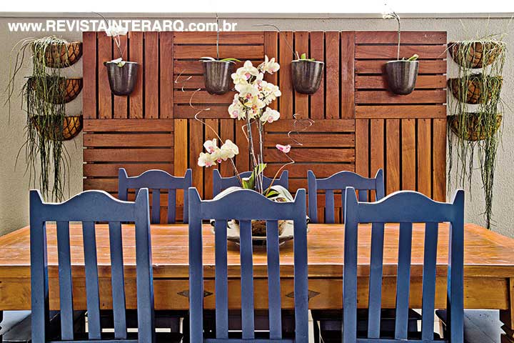 A cor azul royal nas cadeiras oferece frescor à varanda, delimitada pelo painel de madeira natural com orquídeas