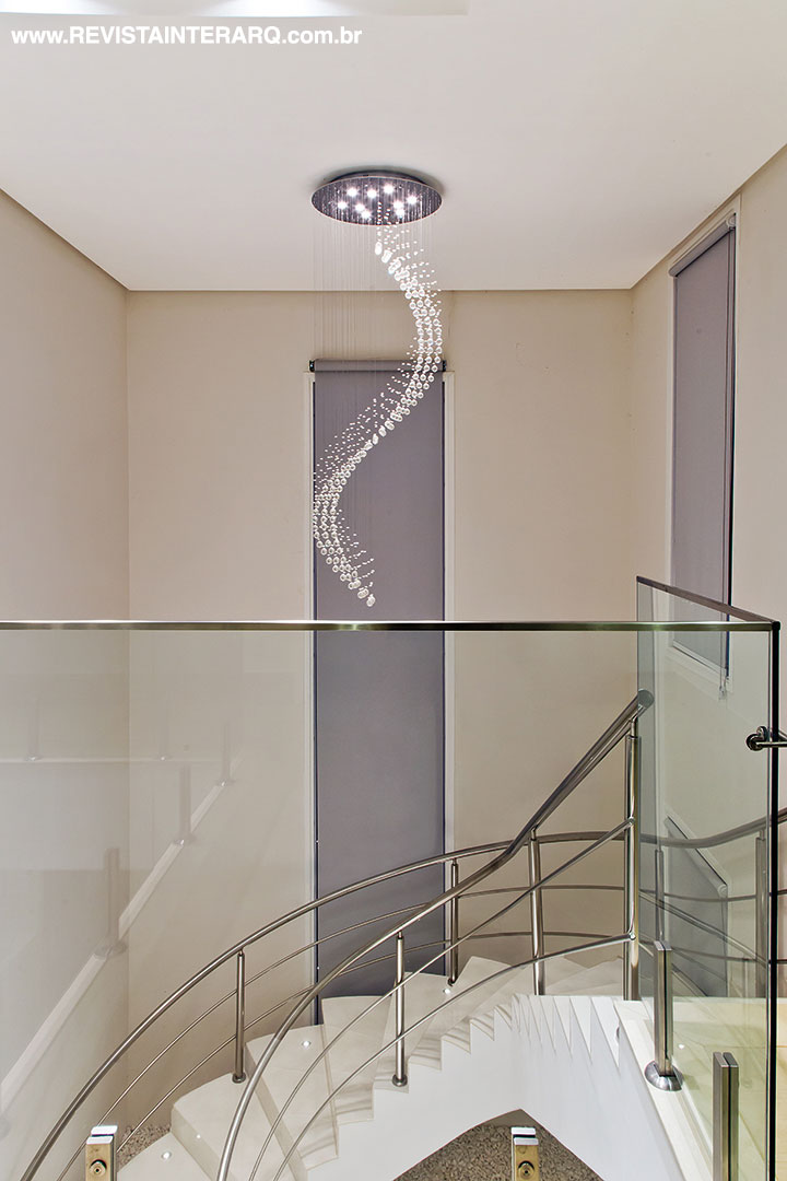 A escada em formato curvo se destaca em meio às paredes ortogonais, como se fosse uma escultura. O pendente de cristal em espiral (Galeria Top Kazza | Saccaro) marca o acesso ao pavimento superior.