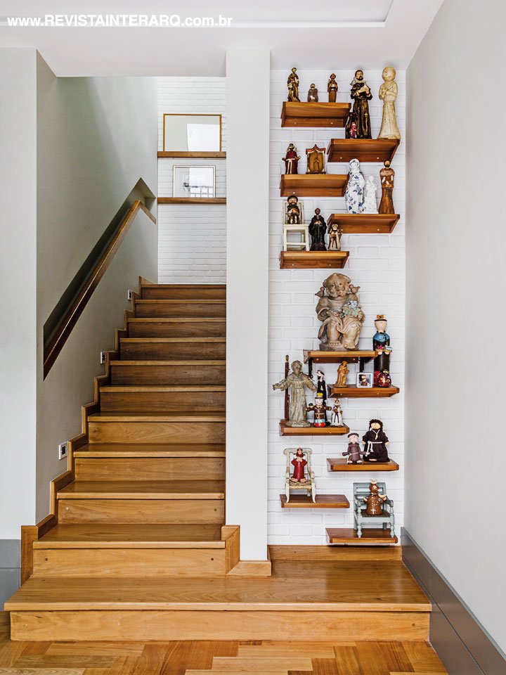 No detalhe da escada em madeira Peroba do Campo, o canto pensado para acomodar a coleção de “São Franciscos” da moradora