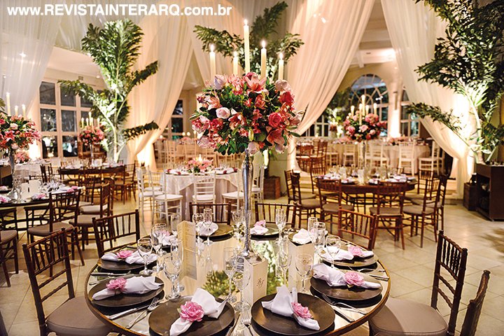 As mesas do salão interno, decoradas com arranjos altos de rosas, lírios e alstroemérias