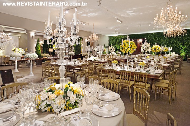O salão com as mesas dos convidados e dos noivos. Nas mesas, sousplats de prata e porta-guardanapos de flor de tecido off-white inspiram romantismo