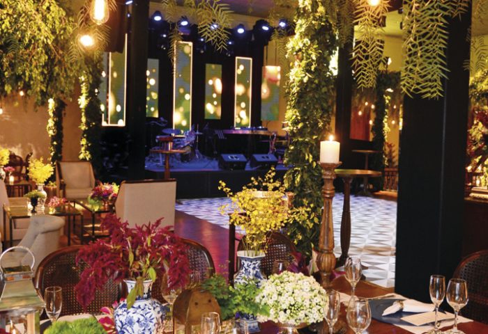 Pontos de luzes suaves e folhagens de diversos tipos pendiam sobre as mesas em madeira (Festah), decoradas com orquídeas chuva-de-ouro, flores brancas (arranjos Juracy Britto), lanternas e cerâmicas (ambos Slaviti). Os cardápios com o menu primoroso (Buffet Dalila) acompanhavam os sousplats azuis. Ao fundo, o palco foi emoldurado com grandes painéis de Led da Célo Led. Os convidados da aniversariante foram recepcionados pelo som da Banda KZar