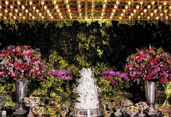 Mini castiçais com velas formavam um “céu estrelado” no pergolado sobre a mesa de doces, emoldurada por orquídeas e um muro inglês (Fest & Cia) no fundo